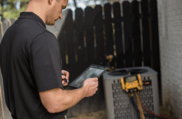 hvac technician looking at ipad while manometer device is connected to outdoor unit in the background