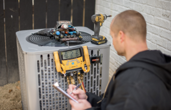 air conditioning technician looking at manometer connected to outdoor hvac unit performing maintenance on the system