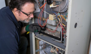 Technician looking over a gas furnace with a flashlight before cleaning it